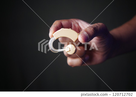 A Hand Holding a Hearing Aid Device for Improved and Enhanced Auditory Assistance Needs 120712702