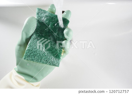Thoroughly cleaning a sponge under running water in the kitchen for effective hygiene 120712757