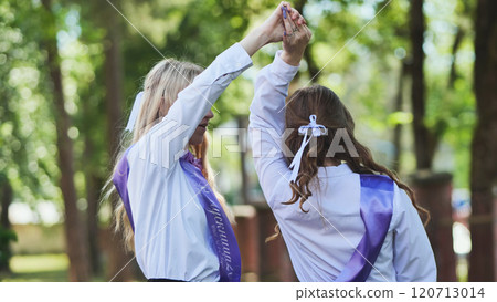 Two girls in purple sashes cheerfully raise their arms in celebration on their final day of school 120713014