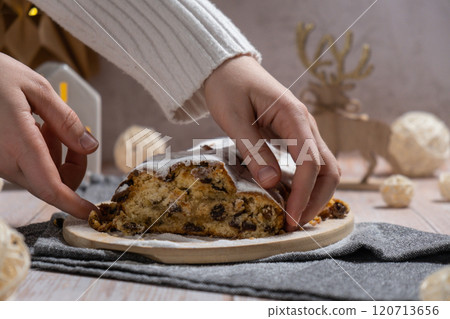 Female hand taking slice of Homemade Christmas traditional cake pie with marzipan nuts and dried fruits pastry dessert stollen. Winter holidays season atmosphere. Delicious tasty composition home 120713656