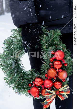 Unrecognizable woman holding Handmade Christmas wreath from red decorations. Festive holiday preparation outdoors in winter snowy weather. Sustainable responsible holiday gift Unrecognizable woman holding Handmade Christmas wreath from red decorations. Festive holiday preparation outdoors in winter snowy weather. Sustainable responsible holiday gift 120713672
