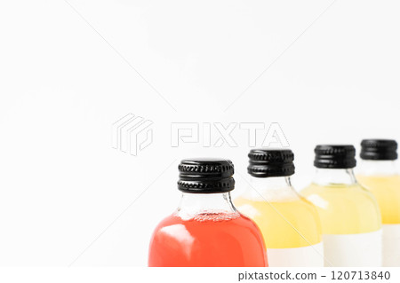 Close up of small transparent glass bottles with black caps, filled with kombucha of yellow and red on a white surface 120713840