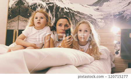 A mom and her two little girls watch TV together in bed A mom and her two little girls watch TV together in bed 120715277