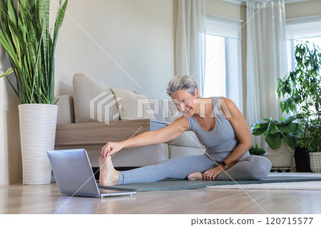 An elderly gray-haired middle-aged woman smiles at her home and plans to do yoga  120715577