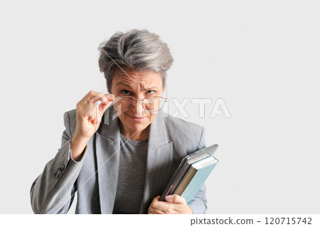 Funny old European woman with gray hair looks over glasses. Laptop and diary. 120715742