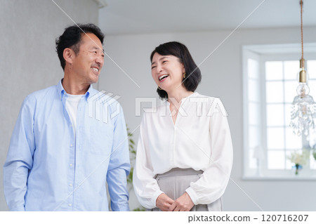 一對微笑的中年夫婦在家裡的客廳消磨時光 一對微笑的中年夫婦在家裡的客廳消磨時光 120716207