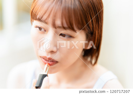 A young woman with a short bob applying lipstick 120717207