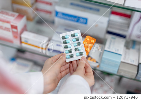 Hands of pharmacist holding medicine capsule blister pack at shelf stocked in pharmacy drugstore. Selecting type of medicine dispensing to patient. 120717940