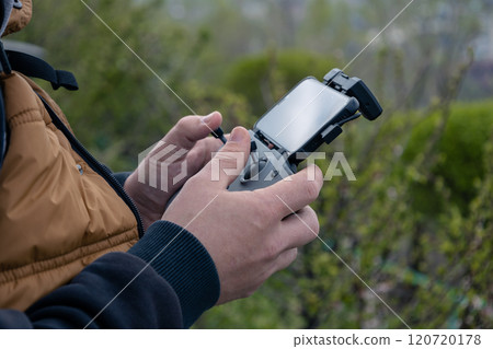 Male hands hold a drone control panel with connected phone. Management by quadcopter flight and videotaping from above Male hands hold a drone control panel with connected phone. Management by quadcopter flight and videotaping from above 120720178