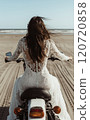 A woman in a wedding dress riding a motorcycle on the beach 120720858