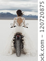 A woman in a wedding dress riding a motorbike in the desert 120720875
