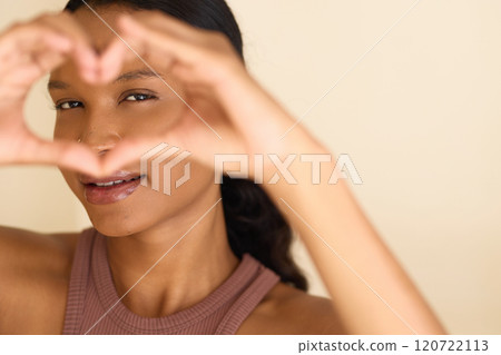 Smiling Woman Framing Face with Heart Gesture in Warm Light 120722113