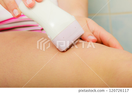 Woman shaving legs with depilator in bathroom Woman shaving legs with depilator in bathroom 120726117