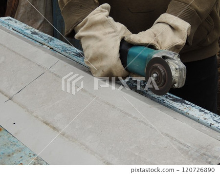 Hands in canvas gloves holding a grinder over a sheet of iron, sawing metal in an outdoor workshop in a village Hands in canvas gloves holding a grinder over a sheet of iron, sawing metal in an outdoor workshop in a village 120726890