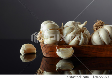 Garlic bulbs in wooden dish on a black background. 120727074