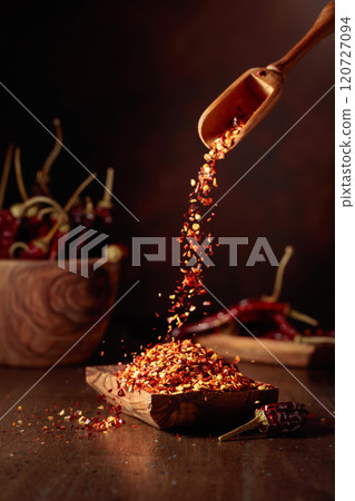 Chilli flakes are poured into a wooden dish. Chilli flakes are poured into a wooden dish. 120727094
