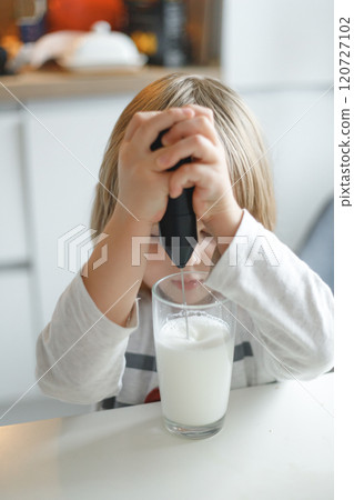 Pre-school child makes frothy milk with a hand mixer in a glass cup in the kitchen Pre-school child makes frothy milk with a hand mixer in a glass cup in the kitchen 120727102