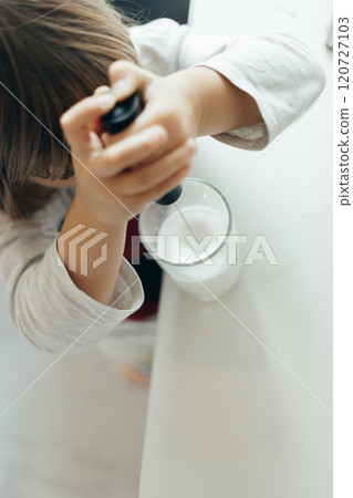 Pre-school child makes frothy milk with a hand mixer in a glass cup in the kitchen 120727103