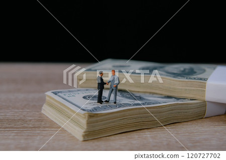 Miniature figures shaking hands on cash. Miniature figures shaking hands on cash. 120727702