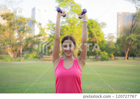 Woman exercising outdoors with dumbbells. 120727767