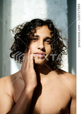 Vertical portrait of multiracial young adult man illumed with sunrays touching his cheek while posing for photo 120727989