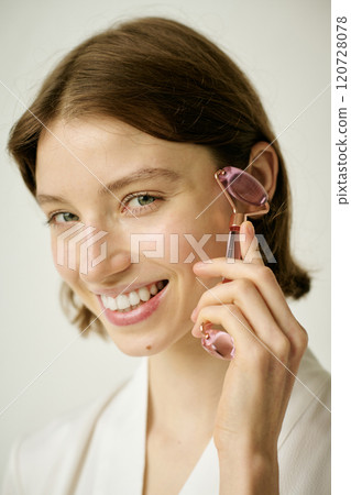 Vertical portrait of young adult woman using rose pink face massager to decrease puffiness and stimulate lymphatic system Vertical portrait of young adult woman using rose pink face massager to decrease puffiness and stimulate lymphatic system 120728078