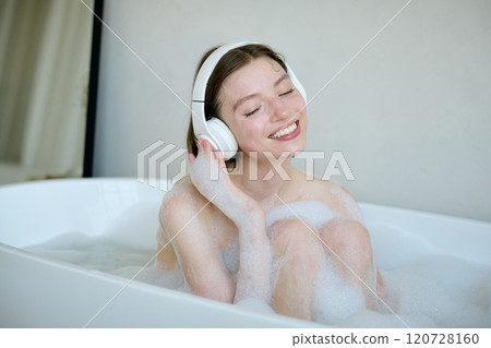 Medium close up of Caucasian woman sitting in white bathtub with water and foam, she listening to music with closed eyes Medium close up of Caucasian woman sitting in white bathtub with water and foam, she listening to music with closed eyes 120728160