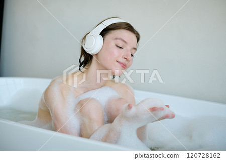 Medium close up of brunette woman playing with foam and listening to music while resting in bathtub Medium close up of brunette woman playing with foam and listening to music while resting in bathtub 120728162