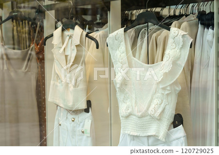 Light-colored women's clothing hangs on display racks behind glass in a shop window 120729025