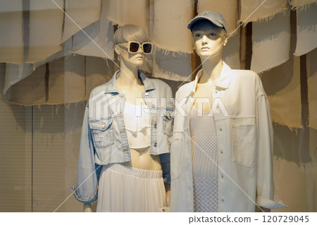 Behind the glass are two female mannequins dressed in a skirt, jacket, glasses and other clothes. Behind the glass are two female mannequins dressed in a skirt, jacket, glasses and other clothes. 120729045
