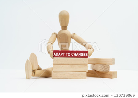 On a white surface sits a wooden man in his hands a block with the inscription - Adapt to Changes On a white surface sits a wooden man in his hands a block with the inscription - Adapt to Changes 120729069