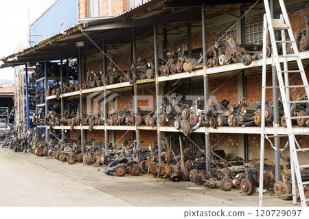 Racks with dismantled spare parts and units from cars stand under a canopy near the building 120729097