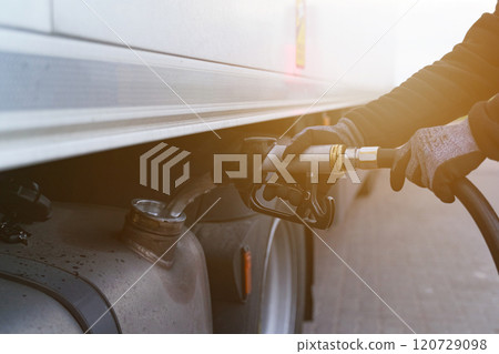 A man holds a gun in his hands, which he inserted into the neck of the fuel tank, refuels the truck. 120729098