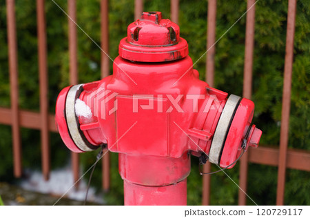 A bright red fire hydrant stands on the street near the fence A bright red fire hydrant stands on the street near the fence 120729117