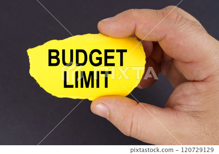 On a black background, in the hands of a man, a yellow torn cardboard with the inscription - budget limit On a black background, in the hands of a man, a yellow torn cardboard with the inscription - budget limit 120729129