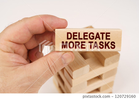 A man holds in his hands a wooden block with the inscription - Delegate More Tasks 120729160