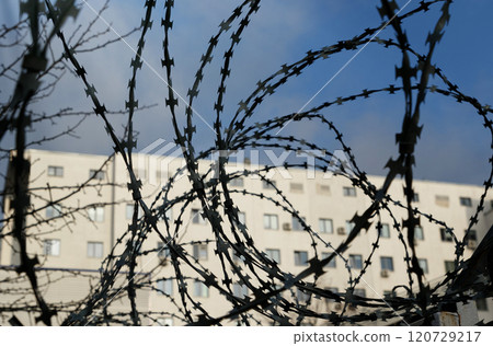 Barbed wire in the foreground, a house and a blue sky in the background in the sun. 120729217