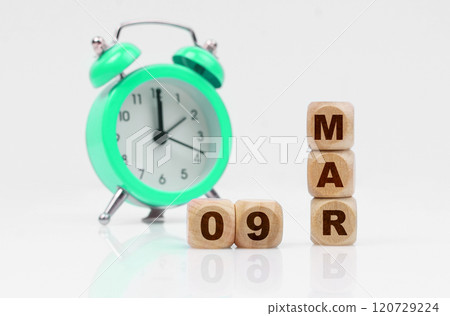 On a white background, a green alarm clock and a calendar with the inscription - March 9 On a white background, a green alarm clock and a calendar with the inscription - March 9 120729224