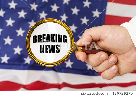 In front of the American flag, a man holds a magnifying glass in his hand with the inscription - Breaking News 120729279