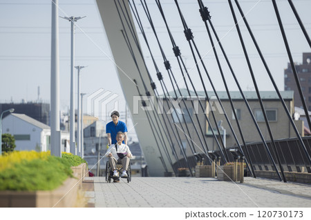 Care staff pushing a wheelchair outdoors 120730173