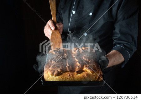 A baker holds a steaming tray of freshly baked bread, its golden crust glistening under the soft glow of kitchen lights. The aroma fills the air, inviting all to savor its warmth A baker holds a steaming tray of freshly baked bread, its golden crust glistening under the soft glow of kitchen lights. The aroma fills the air, inviting all to savor its warmth 120730514
