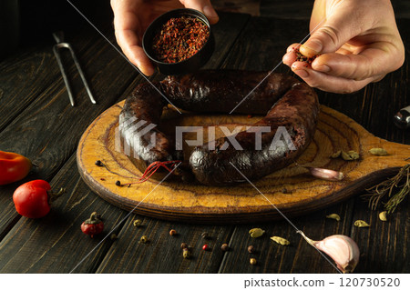 A chef adds dry aromatic spices to blood sausage before serving it for dinner. The sausage sits on a wooden cutting board surrounded by aromatic spices and pepper A chef adds dry aromatic spices to blood sausage before serving it for dinner. The sausage sits on a wooden cutting board surrounded by aromatic spices and pepper 120730520