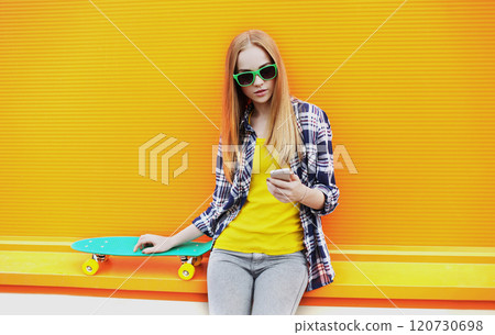 Fashion pretty girl with skateboard using smartphone over colorful orange background Fashion pretty girl with skateboard using smartphone over colorful orange background 120730698