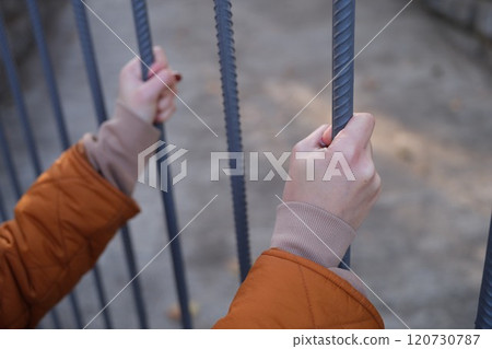 Hands holding tightly onto metal bars, set against a backdrop of tranquility and calmness Hands holding tightly onto metal bars, set against a backdrop of tranquility and calmness 120730787