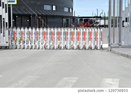 Retractable security gate blocking a road in front of a modern building. Retractable security gate blocking a road in front of a modern building. 120730933