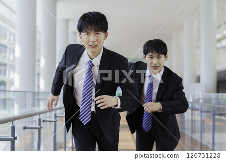 Two young businessmen running through a building corridor Two young businessmen running through a building corridor 120731228
