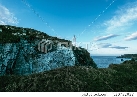 View of lighthouse on rocky coastal cliff beside the ocean under cloudy sky at dusk. View of lighthouse on rocky coastal cliff beside the ocean under cloudy sky at dusk. 120732038