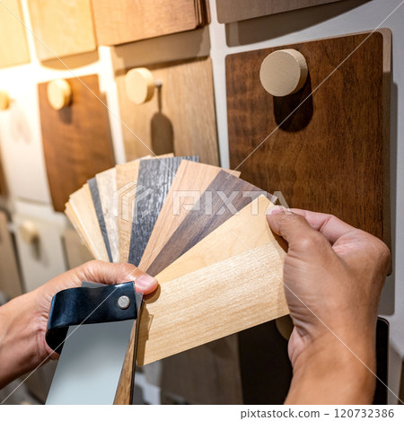 Designer hand picking sample of wood laminated from natural collection in material showroom 120732386