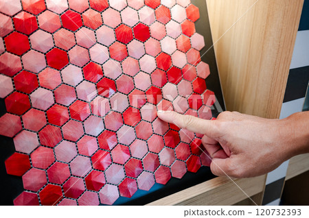 Designer hand pointing at red hexagon pattern mosaic tile on ceramic collection display shelf 120732393