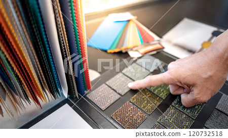 Designer hand pointing at carpet sample pieces with other fabric swatch on the table 120732518